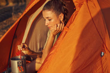 Focused lady cooking tea while sitting in tent