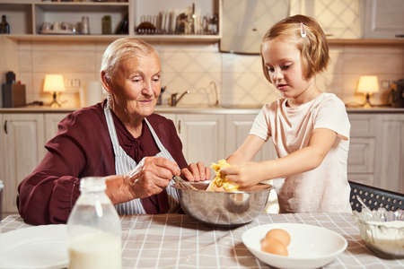 Child kneading dough with hands before her grannyの写真素材