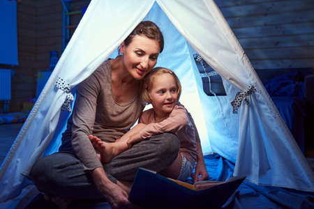 Mother and daughter sitting in tent in bedroomの写真素材