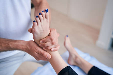 Unrecognized male acupressure specialist working with legs of woman in medical officeの写真素材