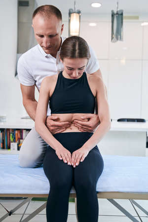 Handsome neat male osteopath examining woman abdomen in medical officeの写真素材