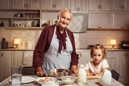 Kind granny standing with her granddaughter in the kitchenの写真素材