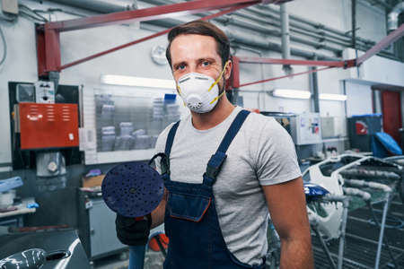 Proud auto mechanic looking at camera with sander in handの写真素材