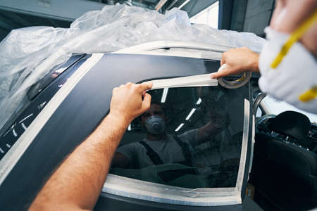 Car service technician sticking duct tape on windowの写真素材