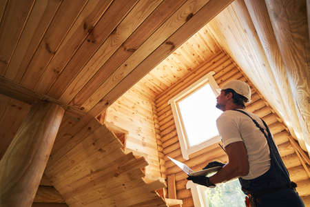 Male worker clicking on laptop while checking house walls