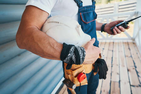 Adult holding walkie talkie and helmet on porchの写真素材