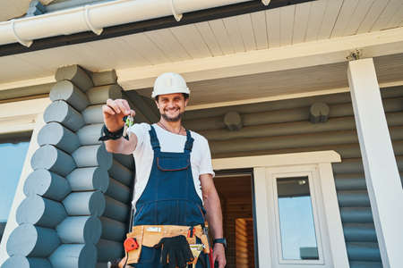 Happy worker standing near house entrance with keysの写真素材