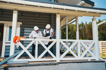 Two male workers on porch inspecting technical document