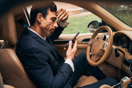 Entrepreneur in car studying his reflection in smartphone screen