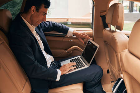 Business specialist using laptop on car passenger seat