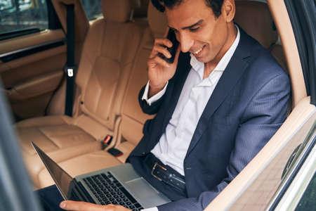 Pleased male executive checking laptop display during a phone callの写真素材