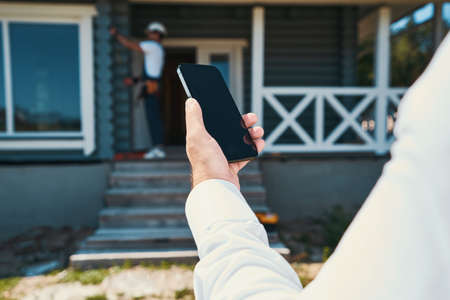 Cropped photo of smartphone in hands of construction workerの写真素材