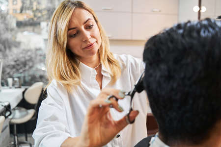 Focused hairdresser trimming hair of her customerの写真素材