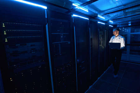 Male server technician walking with laptop in data center roomの写真素材