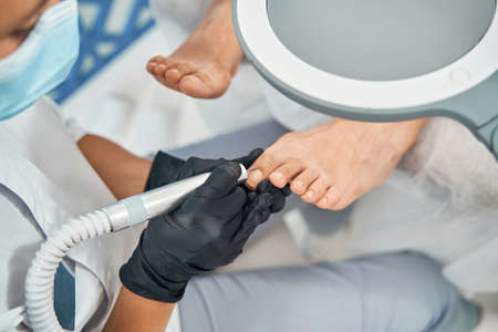 Focused photo on specialist working with nail drillの写真素材