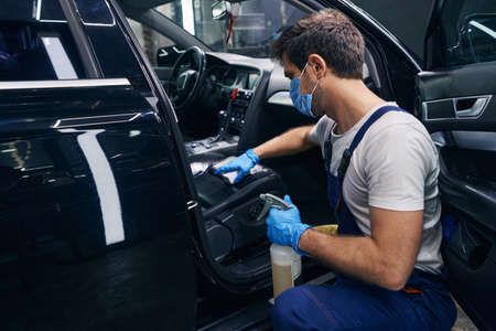 Male wiping seat clean in black car during detailingの写真素材