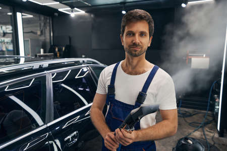Pleased car technician standing with turned-on steam cleanerの写真素材