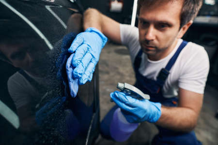 Worker of repair shop cleaning car with dustcloth