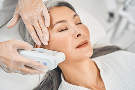 Pleased Asian patient enjoying the procedure of smoothing skinの写真素材