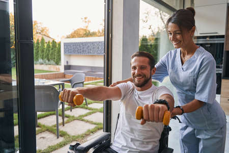 Woman nurse assistant helping to the man with a physical disability in the modern apartments