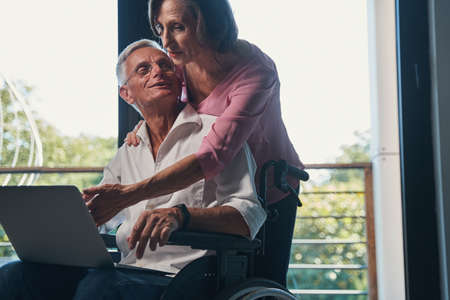 Senior male with disability turning to his wife behind himの写真素材