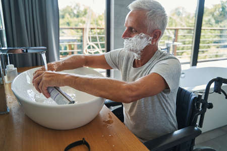 Male wheelchair user washing hands after applying shaving creamの写真素材