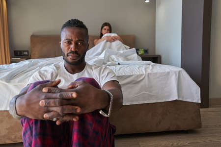 Low-spirited young man and female sitting apart in bedroomの写真素材
