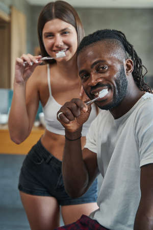Mixed-race couple with toothbrushes in their hands looking aheadの写真素材