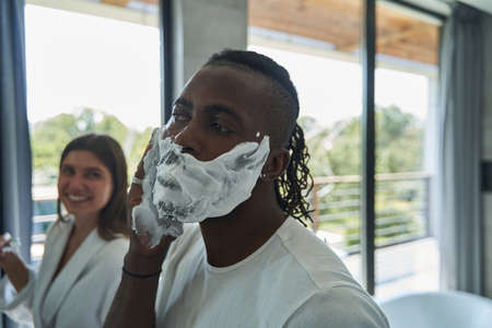 Smiling concentrated female staring at male during his shaving procedureの写真素材