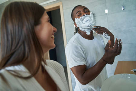 Smiling pleased female observing guy during shaving procedureの写真素材