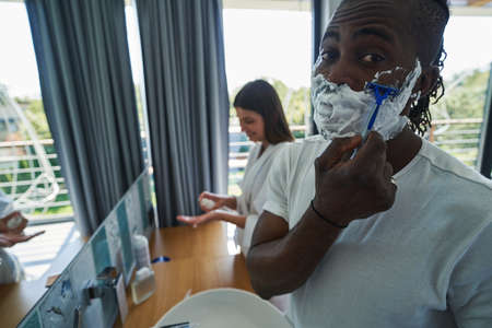 Couple performing personal hygiene procedures before bathroom mirror