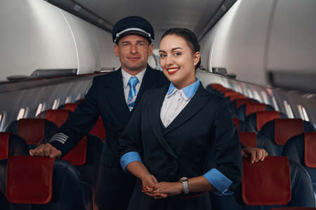 Smiling airplane hostess and captain standing on aisleの写真素材