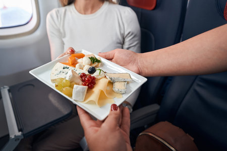 Airline stewardess giving plate with snacks to passengerの写真素材