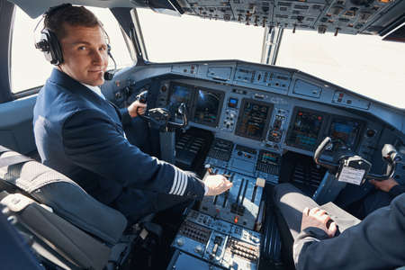 Pleased aircraft captain smiling while pulling thrust leverの写真素材