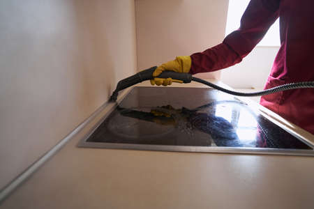 Professional janitor in rubber glove steam-cleaning kitchen counterの写真素材
