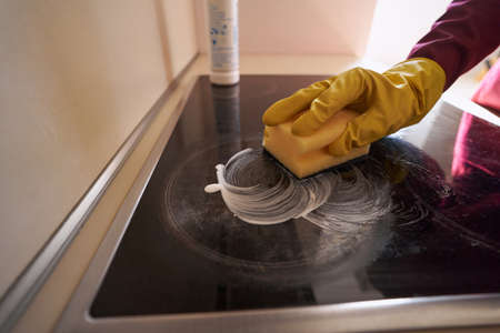 Experienced janitor in rubber glove cleaning cooking surface