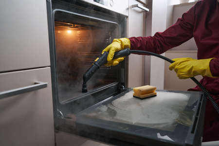 Professional janitor cleaning kitchen appliance with steamの写真素材