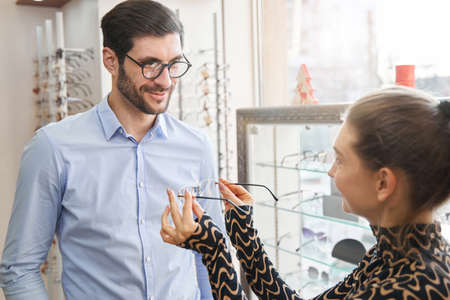 Saleswoman in optical shop offering glasses to pleased clientの写真素材