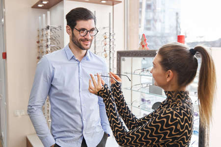 Male buyer at optician shop getting eyeglasses from saleswomanの写真素材