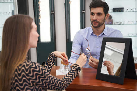 Optician shop worker looking at woman during glasses presentation