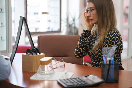 Woman in glasses staring at her face in table mirrorの写真素材