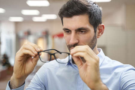 Male buyer in optician shop inspecting pair of glassesの写真素材
