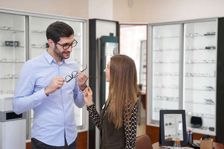 Man picking himself glasses with help of sales assistantの写真素材