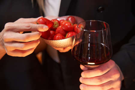 Glass of wine and strawberry in handsの写真素材