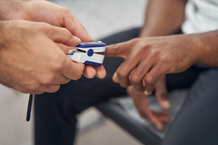 Experienced physician attaching clip of pulse oximeter to male fingerの写真素材