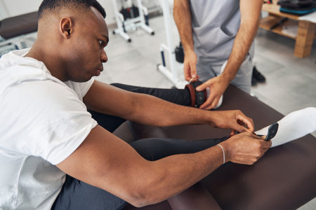Man putting weights on his ankles assisted by physiotherapistの写真素材