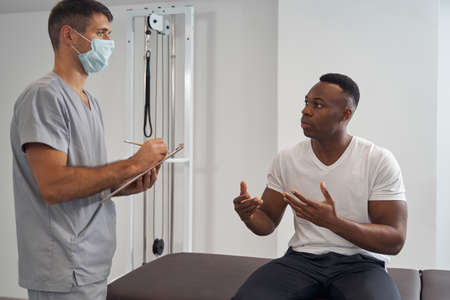 Focused Caucasian physician receiving African American male patientの写真素材