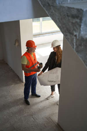 Housebuilder offering cup of coffee to pleased woman engineer