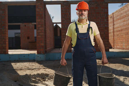 Male housebuilder with two buckets looking at cameraの写真素材