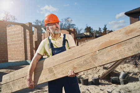 Construction worker carrying a wooden board on siteの写真素材